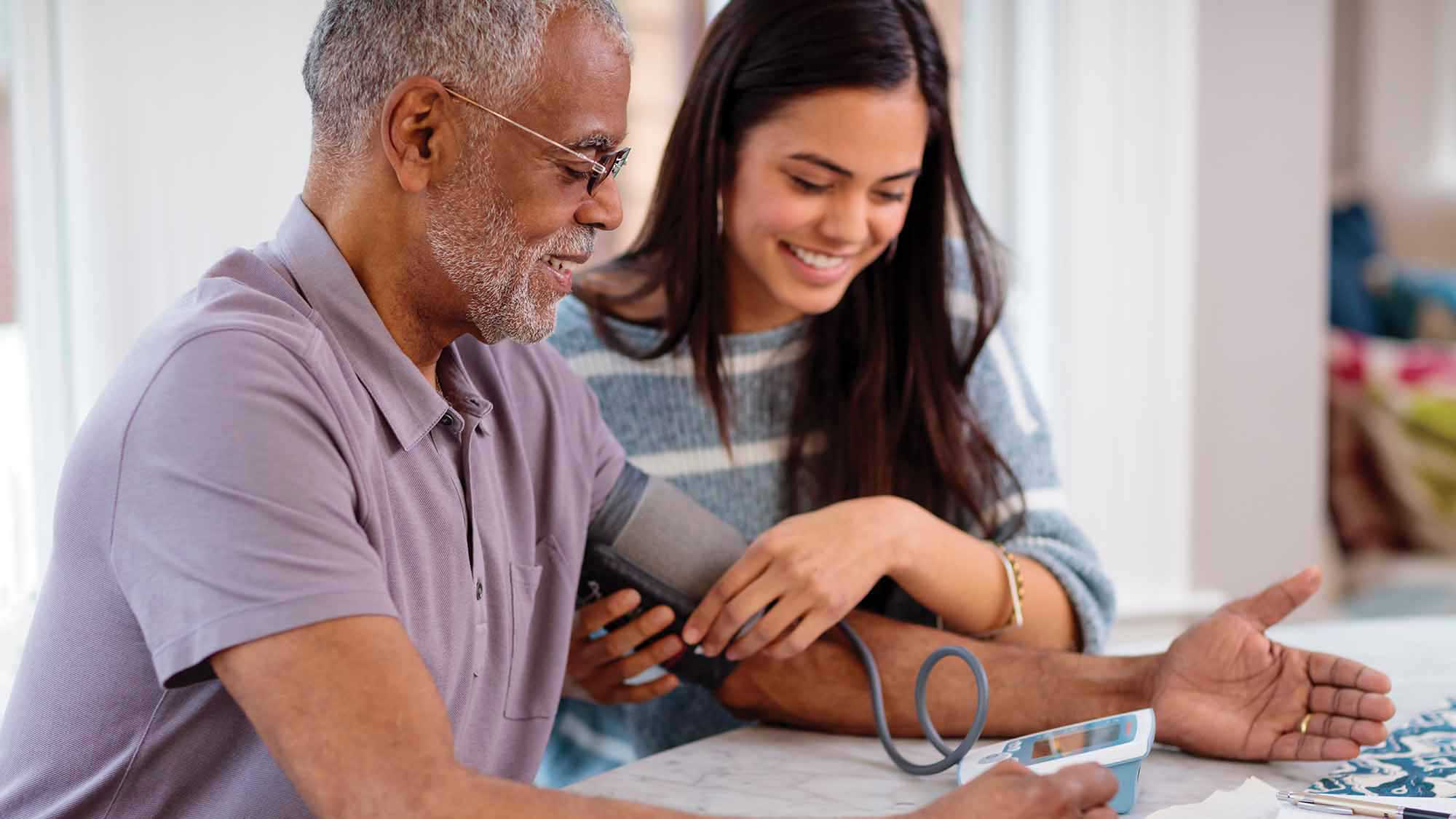A male patient checks his blood pressure with help from an in-home health profressional