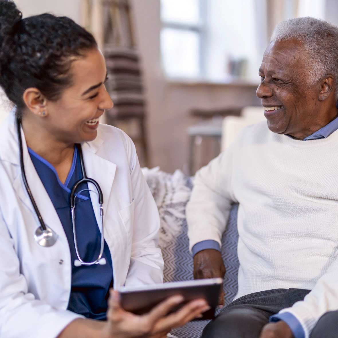 A female practitioner and an elderly male patient engaged in a happy conversation while reviewing health information on a tablet computer